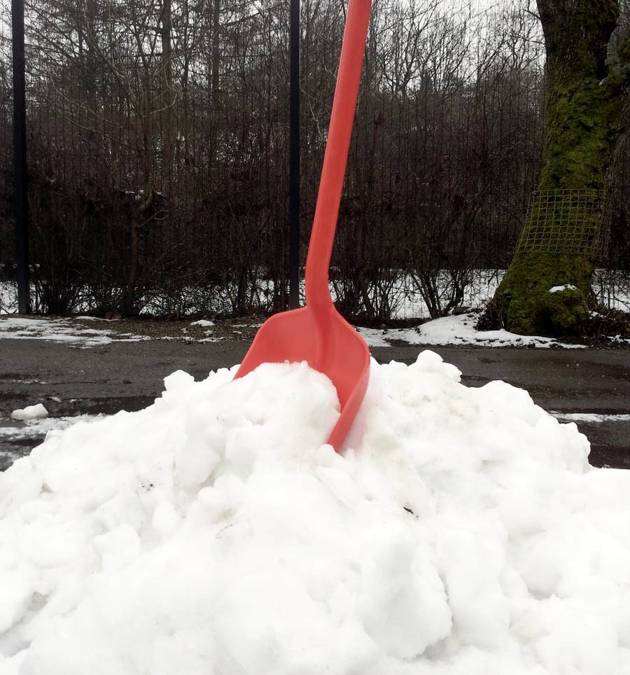 An orange snow shovel standing upright in a fresh pile of snow at the edge of a driveway.