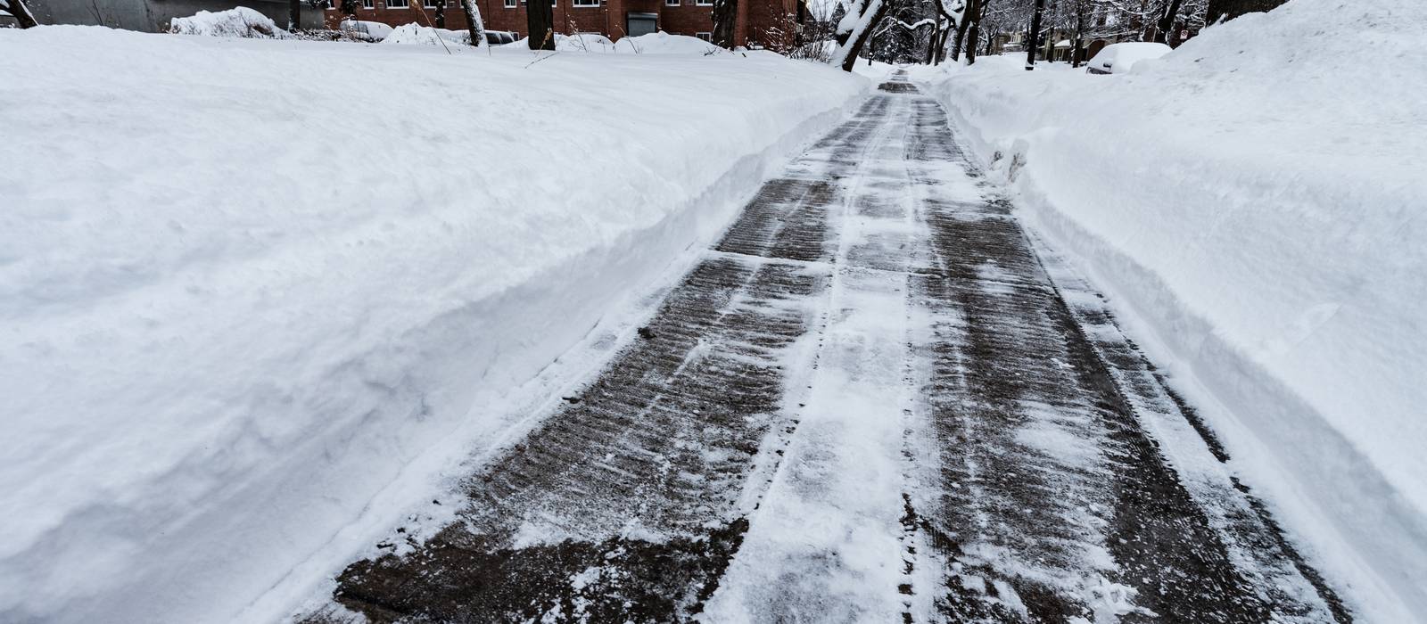 A long sidewalk shoveled clean to the pavement between high banks of snow.